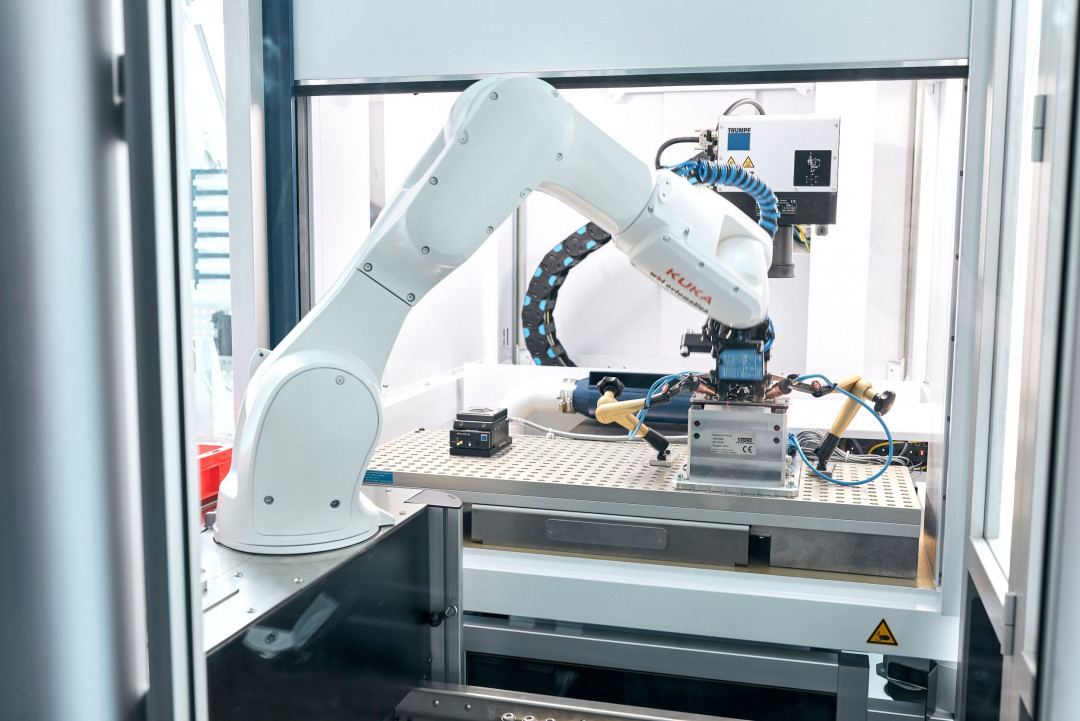 Ein Roboterarm bestückt eine Laserstation: Die Automatisierungslösungen in der Lasertechnik steigern die Produktivität in der Fertigung. - © TRUMPF