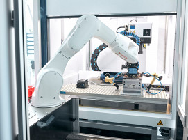 Ein Roboterarm bestückt eine Laserstation: Die Automatisierungslösungen in der Lasertechnik steigern die Produktivität in der Fertigung.