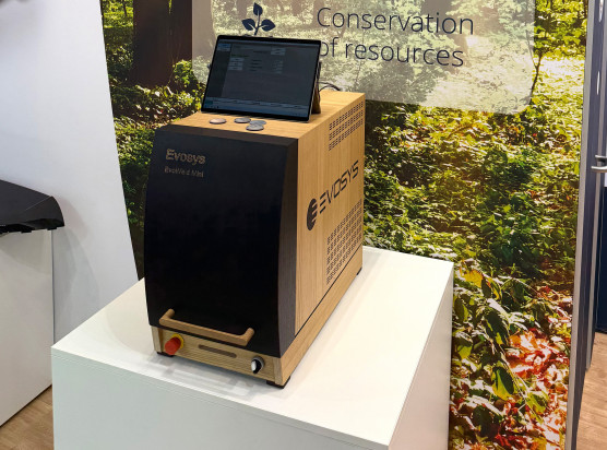 EvoWeld Mini in a wooden case with integrated absorption test function and symbolic significance for the sustainability aspect of laser plastic welding.